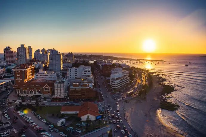 the sun is setting over a city by the ocean